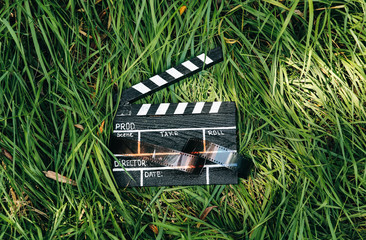 Black clapperboard with film lying on the grass in the nature outdoors. Directing and of amateur...