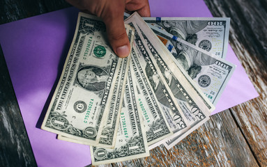 Man is holding dollar banknotes with on the purple pastel background. Money notes on the surface....