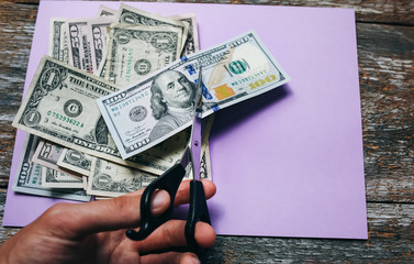 Man is cutting dollar banknotes with scissors on the purple pastel background. Money notes on the...