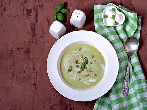 Cream of green pea soup, sprinkled with pumpkin seeds, in a white plate. Served with mozzarella cheese. Top view.