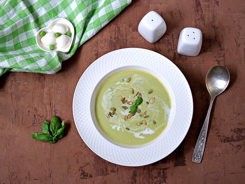 Cream of green pea soup, sprinkled with pumpkin seeds, in a white plate. Served with mozzarella cheese.