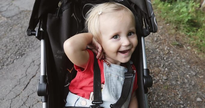 A cute little girl is sitting in the pram outdoors. Happy baby smiling.
