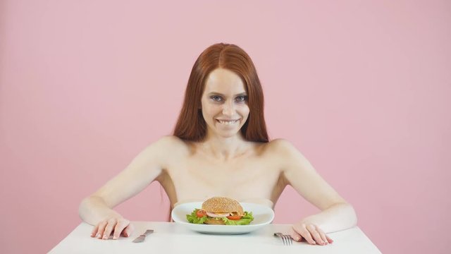 Happy anorexic girl struggles with the temptation to eat a Burger.