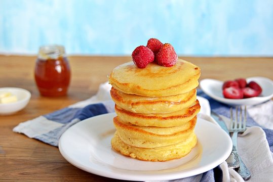 Cornmeal pancakes on a white plate. Served with frozen strawberries and honey or maple syrup.