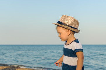 Fototapeta na wymiar Little girl in a hat walks along the seashore