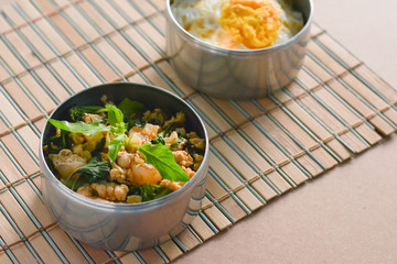 Thai basil chicken in round metal bowl on wooden table.