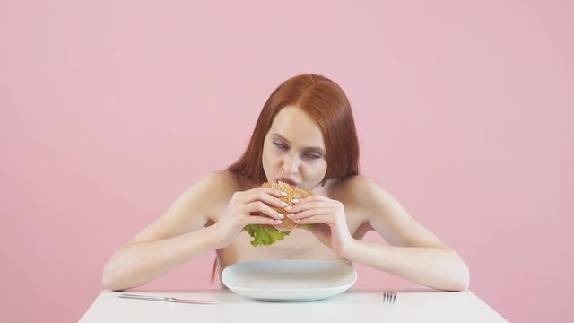 Happy anorexic girl greedily eating a Burger. Violation of diet. Anorexia.