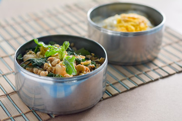 Thai basil chicken in round metal bowl on wooden table.
