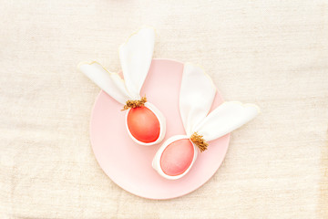 Easter bunny (rabbit) egg concept, table arrangement decoration. Pink (rosy) eggs with plate on...