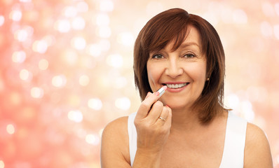 beauty, make up and old people concept - smiling senior woman applying lipstick to her lips over...