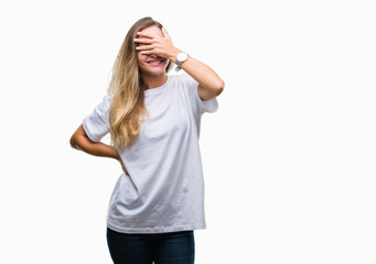 Obraz na płótnie Canvas Young beautiful blonde woman wearing casual white t-shirt over isolated background smiling and laughing with hand on face covering eyes for surprise. Blind concept.