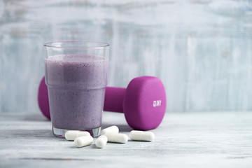 Glass of Protein Shake with milk and blueberries. BCAA amino acids and a violet dumbbell in background. Sport nutrition. Rustic wooden background. Copy space. 