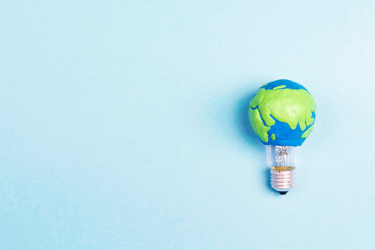 Light bulb with plasticine Earth planet model on blue background with space for text.