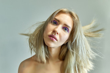 Closeup portrait concept of a beautiful blonde girl on a gray background. Hair develops in different directions.