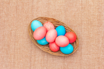 Easter eggs concept, table arrangement decoration. Pink (rosy) and blue eggs in wicker basket on cloth (linen) background, top view