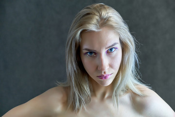 Closeup portrait concept of a beautiful blonde girl on a gray background. Hair develops in different directions.