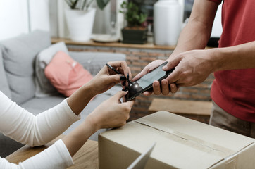 home delivery service man in red uniform and young woman customer appending signature in digital mobile phone receiving parcel post box from courier at home, express delivery, online shopping concept