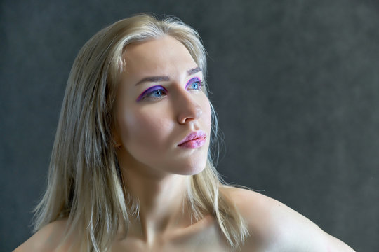 Closeup portrait concept of a beautiful blonde girl on a gray background. Hair develops in different directions.