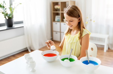 easter, holidays and people concept - happy girl coloring eggs by liquid dye at home