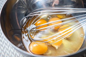Broken eggs before cooking in a steel bowl and whisk