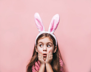 Cute little girl with bunny ears on pink background. Easter child portrait, funny emotions, surprise. Copyspace for text.