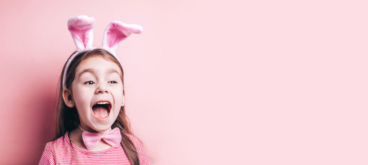 Cute little girl with bunny ears on pink background. Easter child portrait, funny emotions, surprise. Copyspace for text.