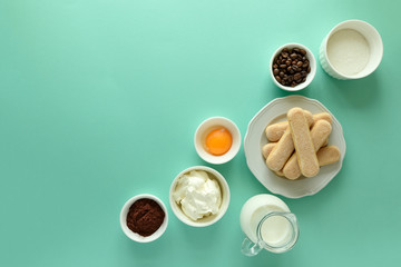Ingredients for cooking tiramisu: sponge fingers cookies (Savoiardi, Ladyfinger, biscuit), mascarpone, cream, sugar, cocoa, coffee and egg on blue background. Top view. Flat lay