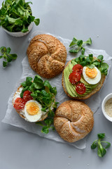 Bagel sandwiches with cream cheese, avocado, tomatoes, egg and greens on gray wooden background. Selective focus. Healthy eating or vegetarian food concept