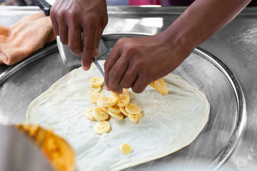 Cooking traditional Thai fried roti banana pancakes close up, asian street food preparation in Thailand, man chef hands frying pancakes on griddle in Bangkok, sweet fruit banana roti making on hot pan