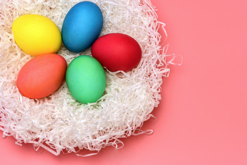 Fototapeta na wymiar Five Easter colored eggs lie in the nest on a gently pink background, top view. Horizontal photo. .
