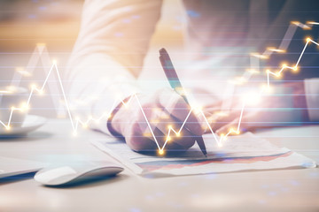 Close up of hands writing with double exposure of business charts. Financial concept.