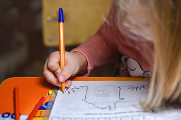 Child preschooler learns to draw and write in notebooks at home in the evening under the light from a desk lamp.