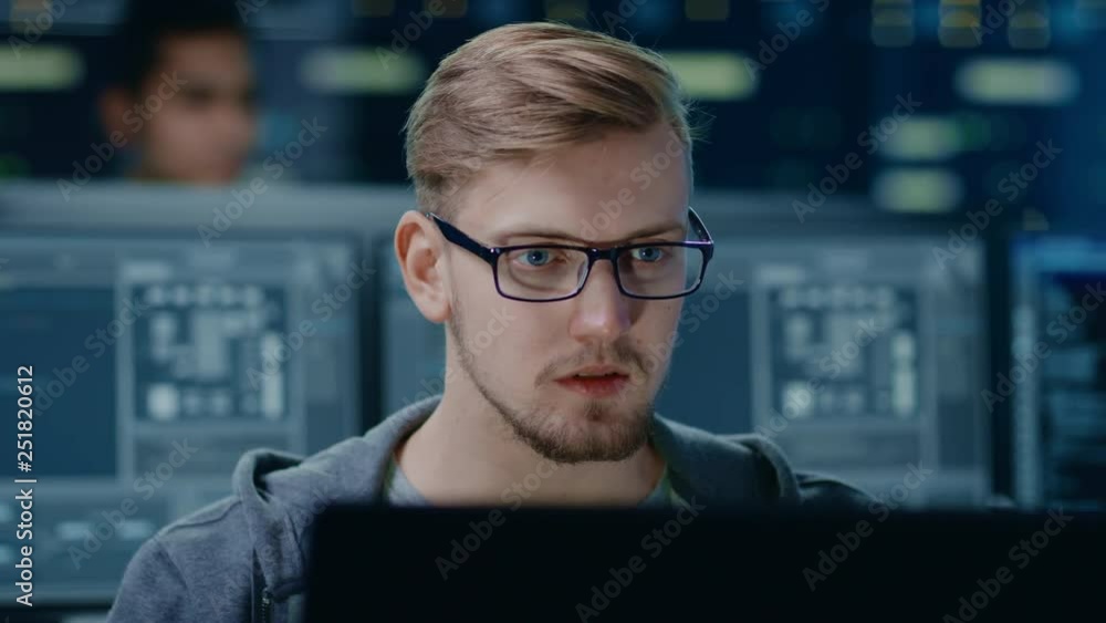 Poster Portrait of a Smart and Handsome IT Specialist Wearing Glasses Works on a Personal Computer. In the Background Unfocused Personal Computers with Screens in Technological Research Data Center