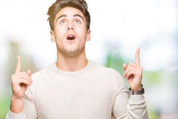 Young handsome man over isolated background amazed and surprised looking up and pointing with fingers and raised arms.