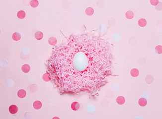 Three eggs in paper pink nest on pink table with confetti. Top view, flat lay
