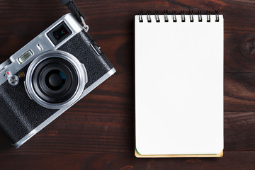 Blank notepad page and modern camera in classic style on dark brown wooden table