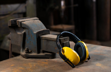 Yellow safety ear protection resting on an iron workshop vice bolted to a workbench