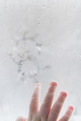 The child's hand draws a man on a frozen misted window in winter