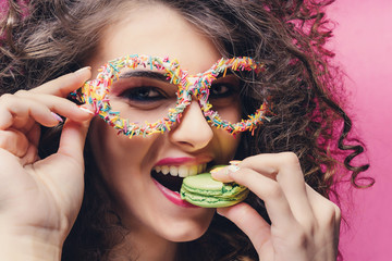 Beautiful girl eat green macaroon and smile in confectionery dressing glasses