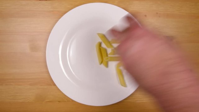 Greedy hand takes plain pasta from plate with bare hand.