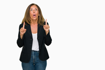 Obraz premium Beautiful middle age business adult woman over isolated background amazed and surprised looking up and pointing with fingers and raised arms.