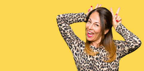Beautiful middle age woman wearing leopard animal print dress Posing funny and crazy with fingers on head as bunny ears, smiling cheerful