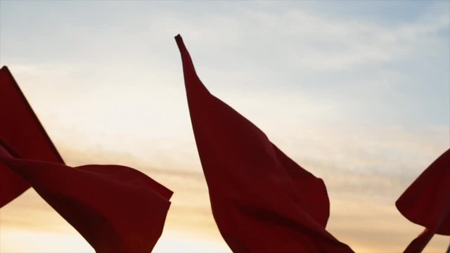 Hands of a group of people waving red flags against sunset.