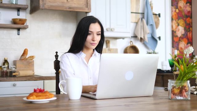 Young Woman Using Laptop While Drinking Morning Coffee In Kitchen