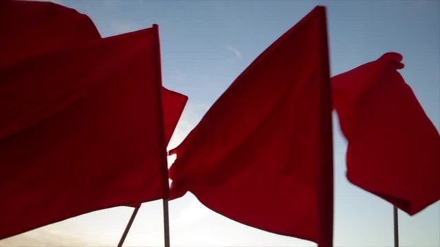 Crowd waving red flags against blue sky.