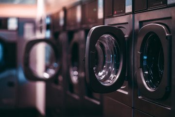 A dark room of a publiс laundry with a row of empty washing machines inside, selective focus on...