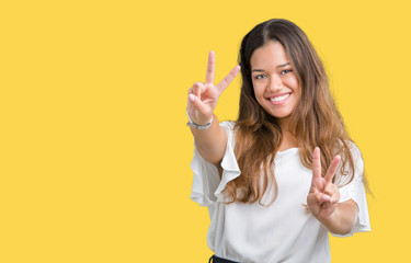 Young beautiful brunette business woman over isolated background smiling looking to the camera showing fingers doing victory sign. Number two.
