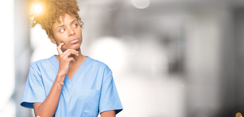 Young african american doctor woman over isolated background with hand on chin thinking about question, pensive expression. Smiling with thoughtful face. Doubt concept. - Powered by Adobe