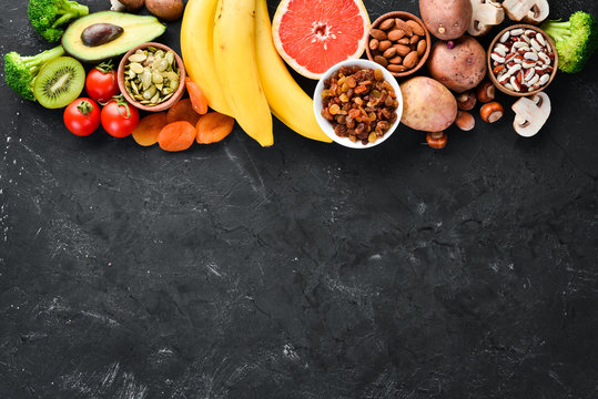 The food contains natural potassium. K: Potatoes, mushrooms, banana, tomatoes, nuts, beans, broccoli, avocados. Top view. On a black background.