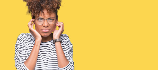 Beautiful young african american woman wearing glasses over isolated background covering ears with fingers with annoyed expression for the noise of loud music. Deaf concept.